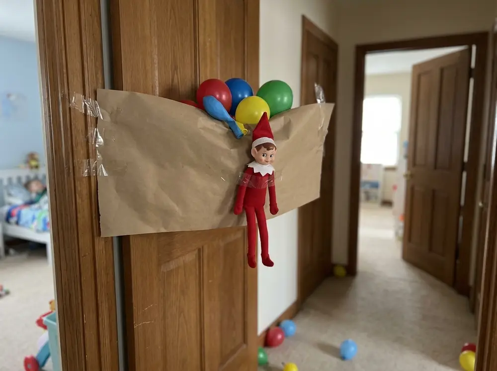 Tape a paper sheet over the top third of the child's doorway, fill it with a few balloons, elf taped alongside — it dumps when the door opens