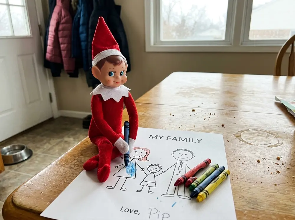 Set the toy elf doll at the table with crayons and a stick-figure drawing of the family, signed with the toy elf doll's name