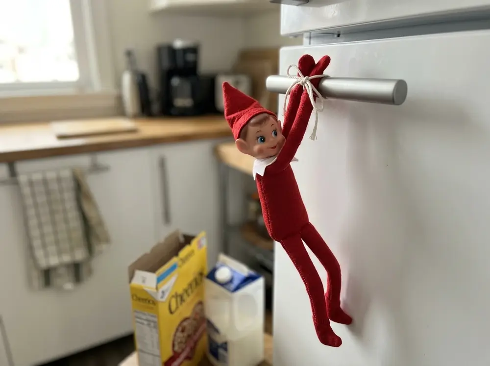 Tie the toy elf doll's arms over the fridge door handle so it hangs where breakfast starts
