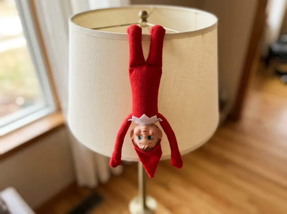 Toy elf doll dangling upside down from a lampshade