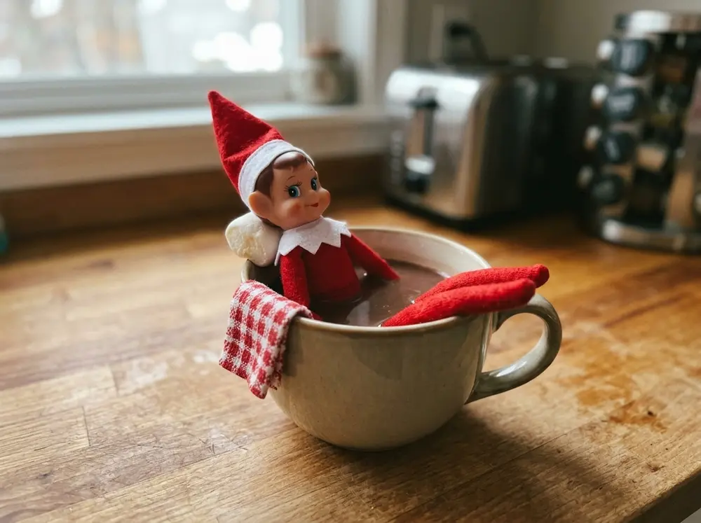Toy elf doll lounges in a mug 'hot tub' with a marshmallow pillow and a washcloth towel folded on the rim