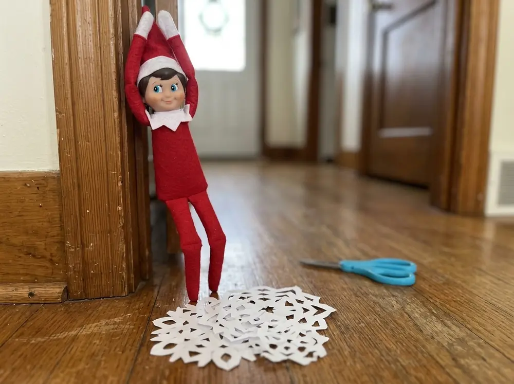 Cut three or four paper snowflakes, scatter them under the toy elf doll hanging from a doorframe with the scissors nearby (out of reach)