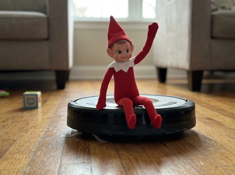 Toy elf doll riding a robot vacuum across a hardwood floor