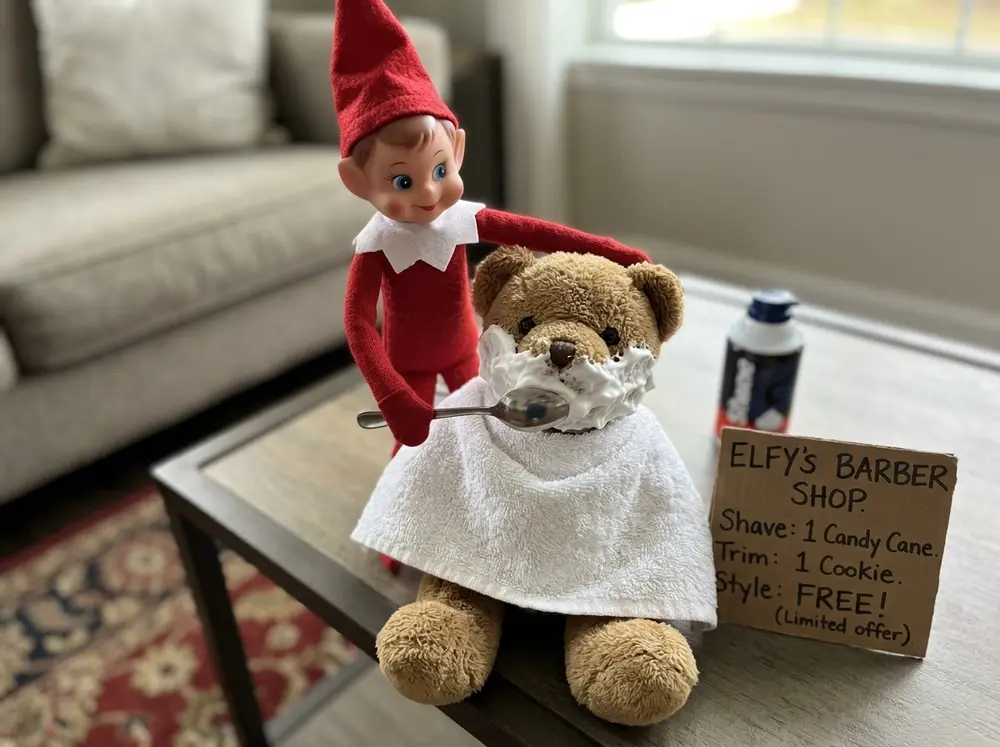 One brave plush sits draped in a towel with a shaving-cream 'lather' beard; the toy elf doll stands behind it with a spoon 'razor' and a price list