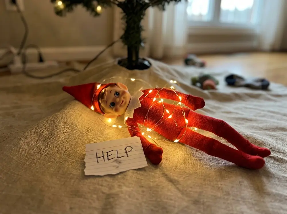 Toy elf doll tangled in glowing fairy lights next to a tiny help sign