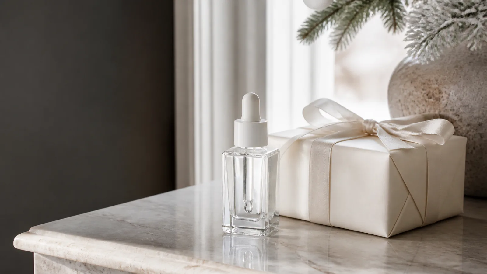 Representative clear luxury serum bottle beside an ivory Christmas gift