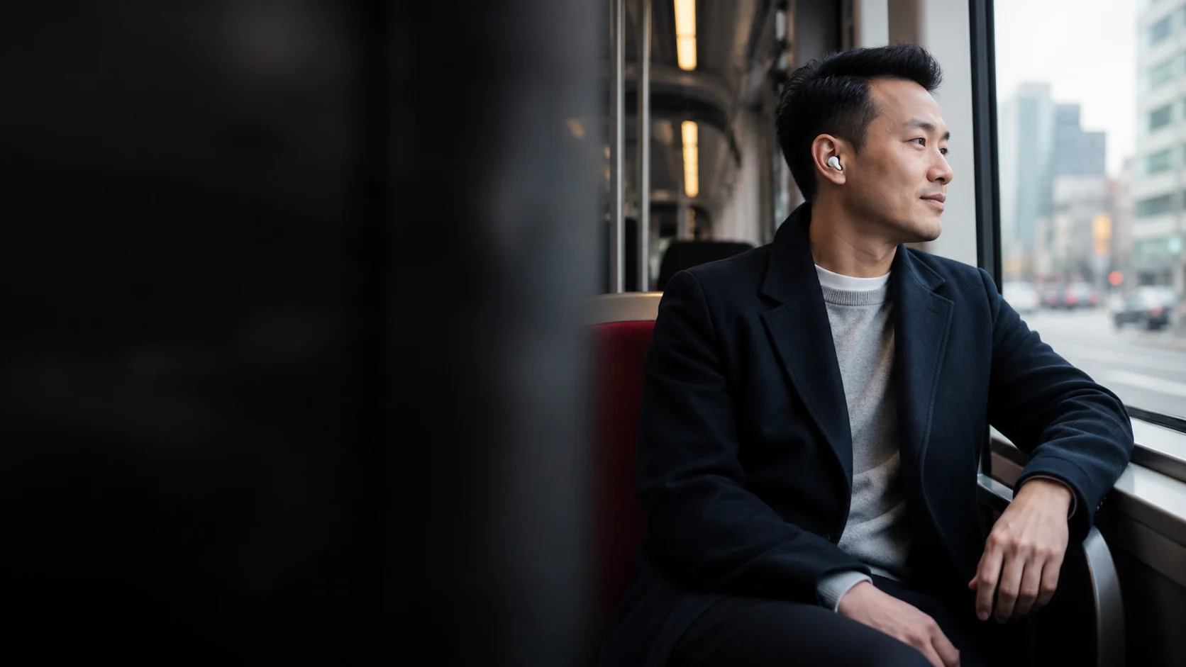 Representative commuter wearing open-fit wireless earbuds on public transit